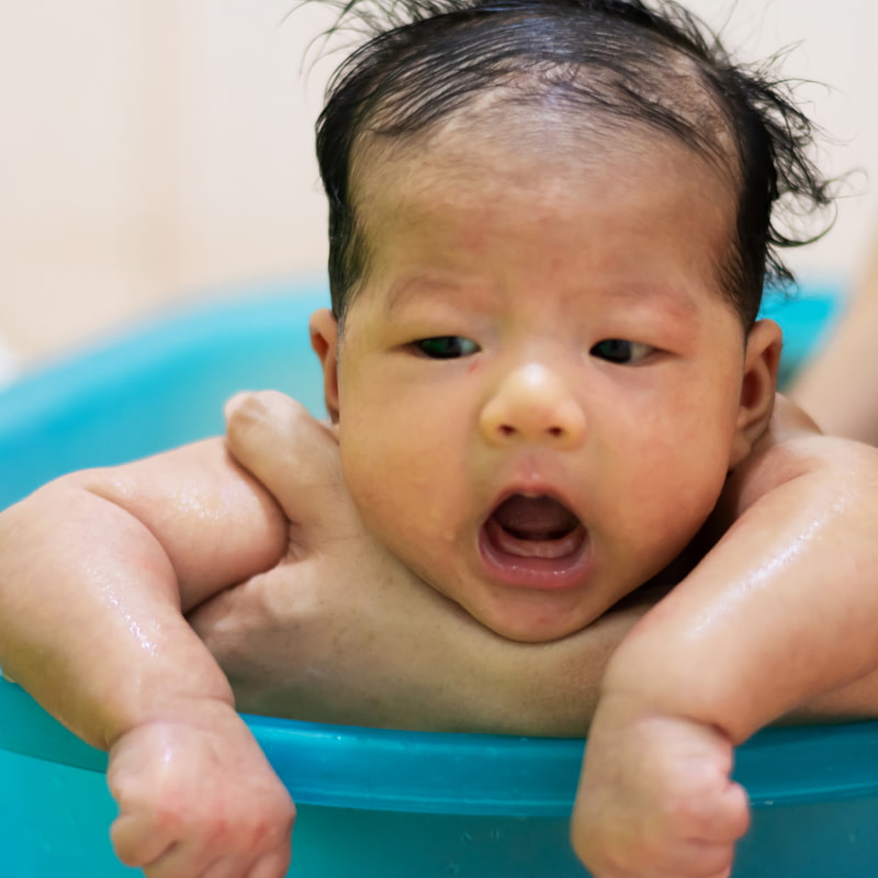 Image of a parent supporting a baby in a baby bath.