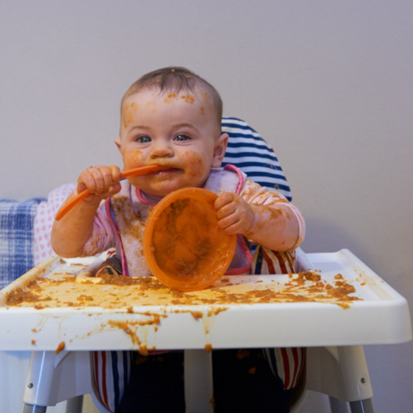 baby in highchair holding bowl