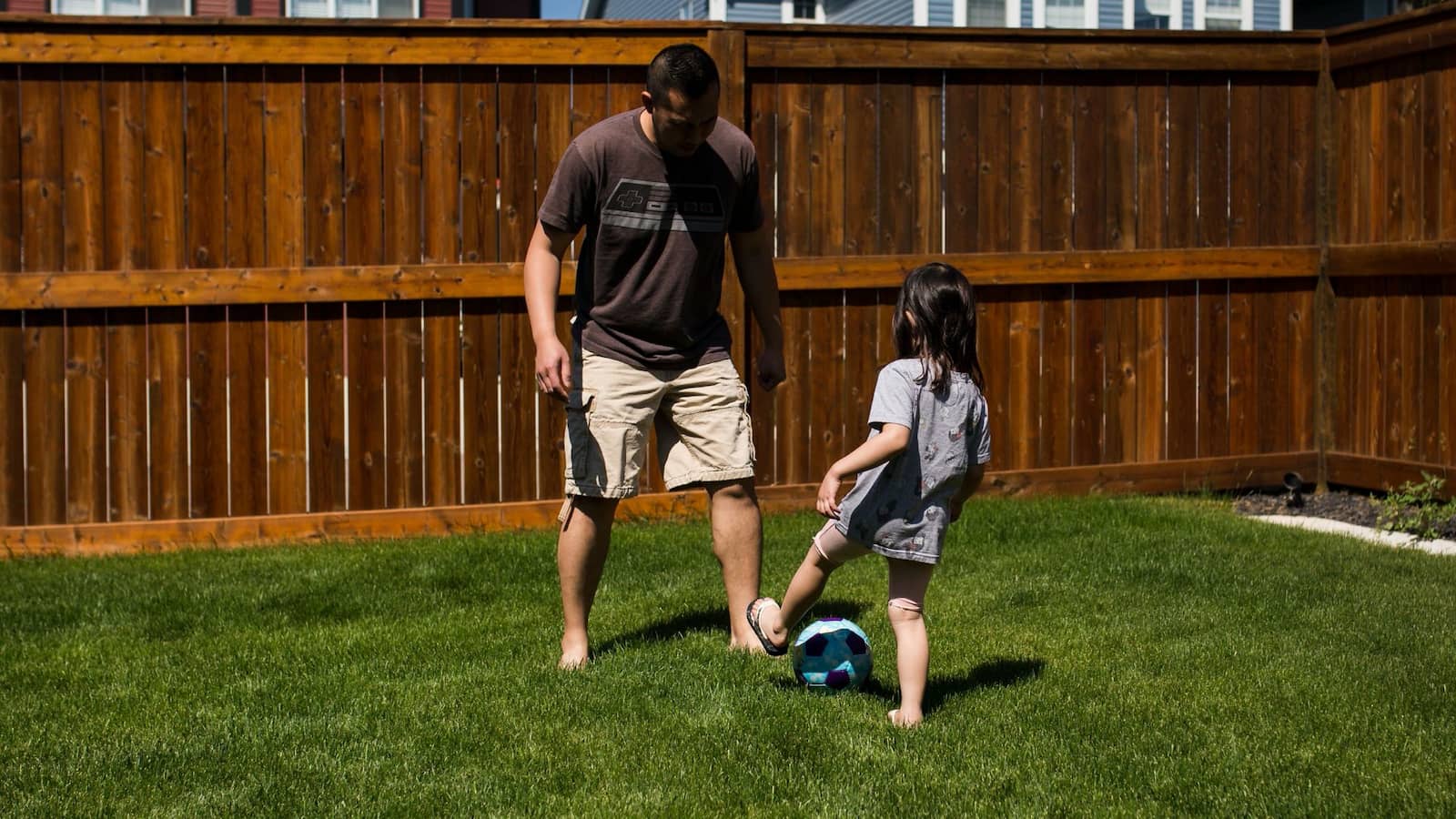 Image of a child and dad playing football in a garden.
