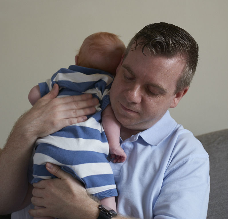 Image of a dad holding a baby on his shoulder.