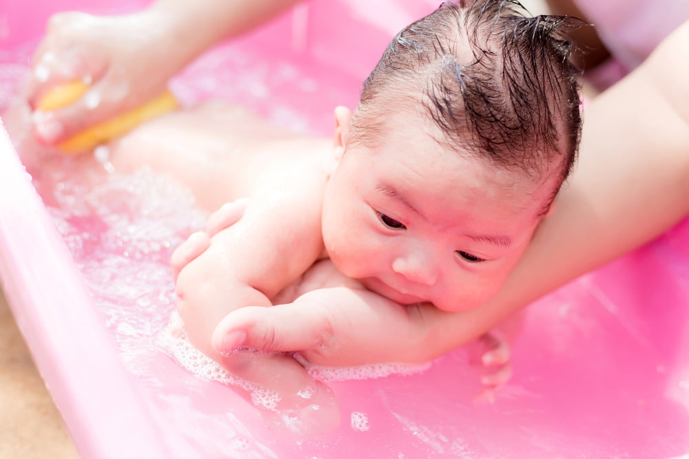 Image of a mum bathing a baby in a pink bath.