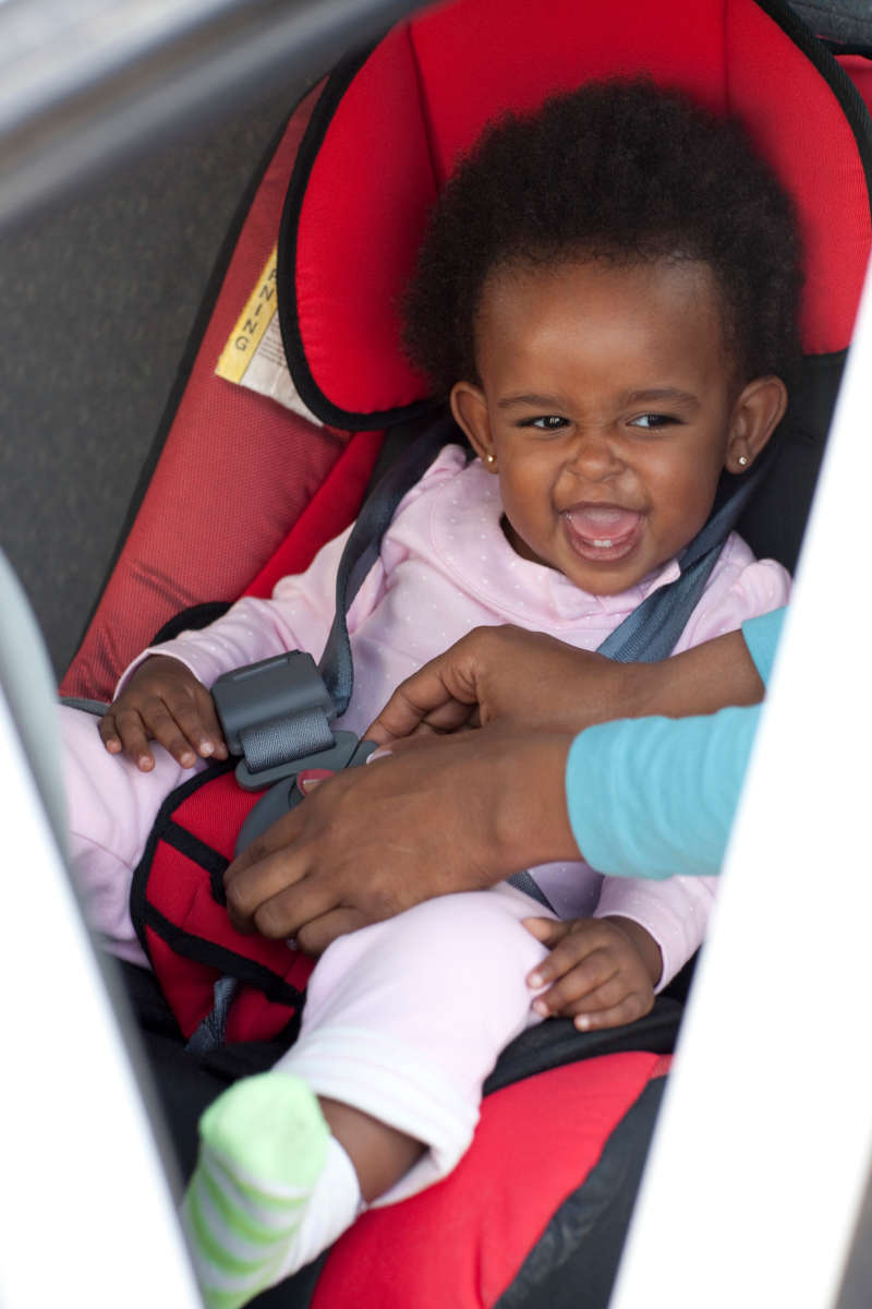 Image of a mum's hands buckling a toddler's carseat belt in a car.