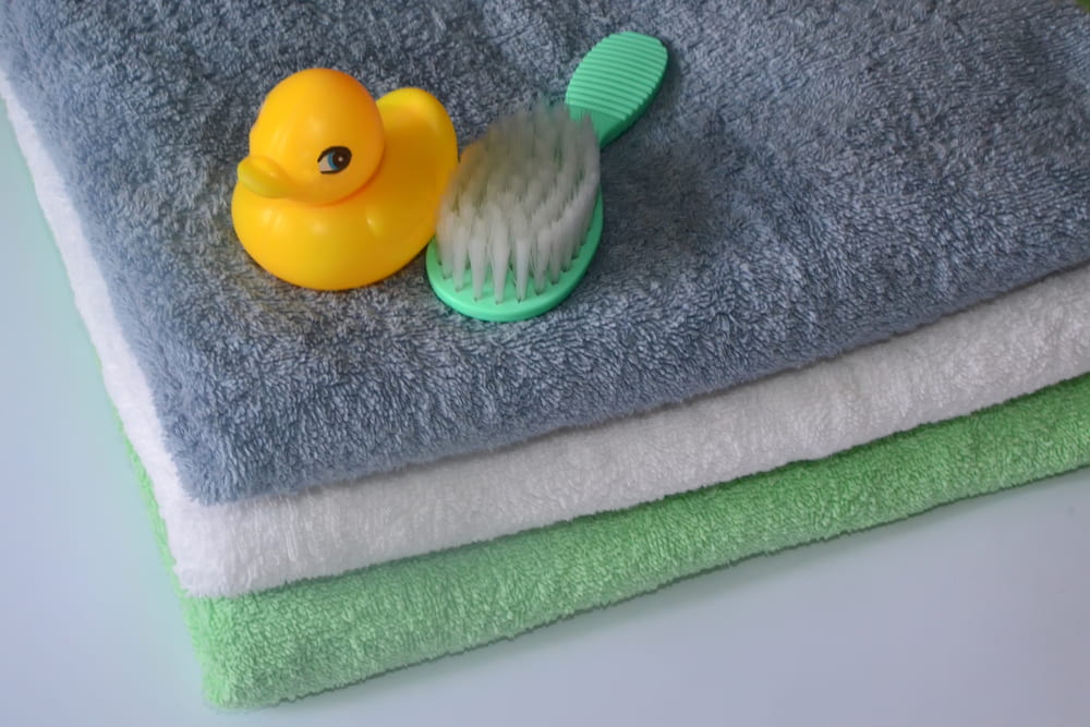 Image of three folded towels with a rubber duck and a hairbrush on top of the pile.