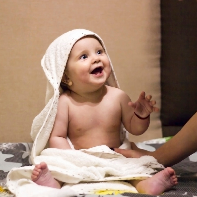 Image of a smiling baby sitting in a towel and looking up at a parent off-camera.