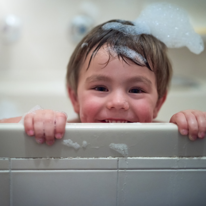 Image of a toddler smiling at the camera with bath bubbles in their hair.