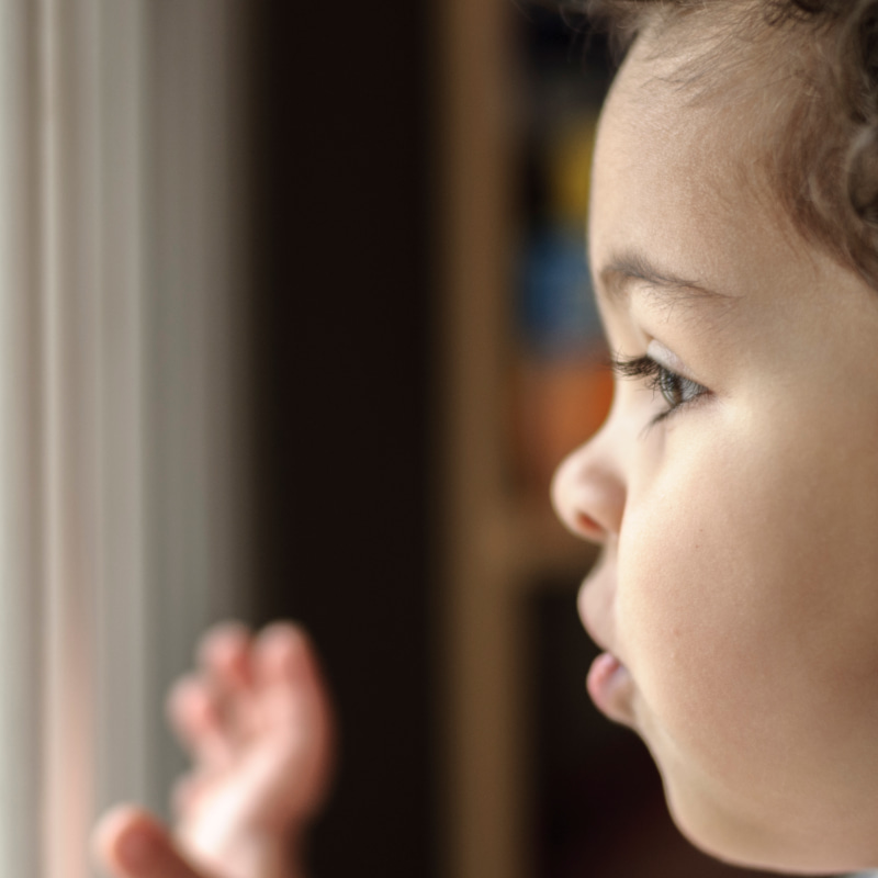 Image of a toddler looking out of a window and waving.