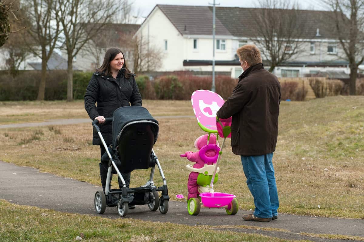 Image of two adults walking in a park, each with a pram.