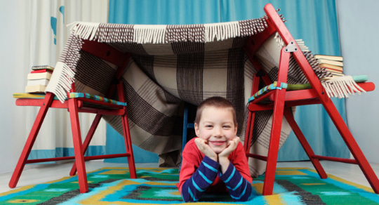 Photo of a boy sitting under a blanket fort 