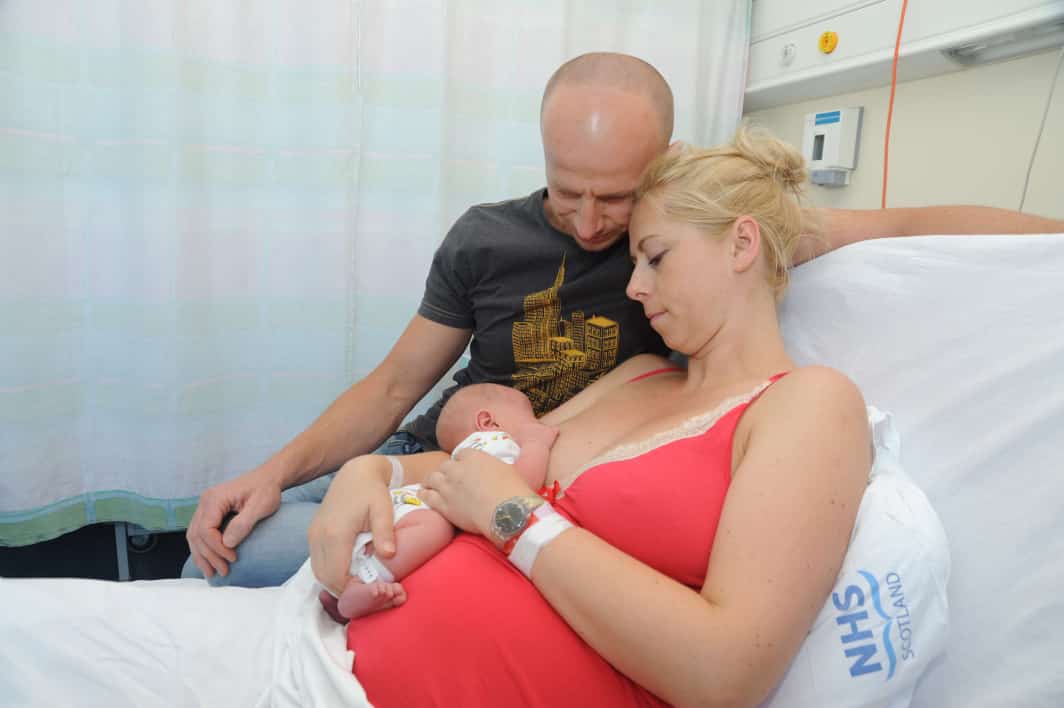 Photo of parents looking at their newborn who is breastfeeding 